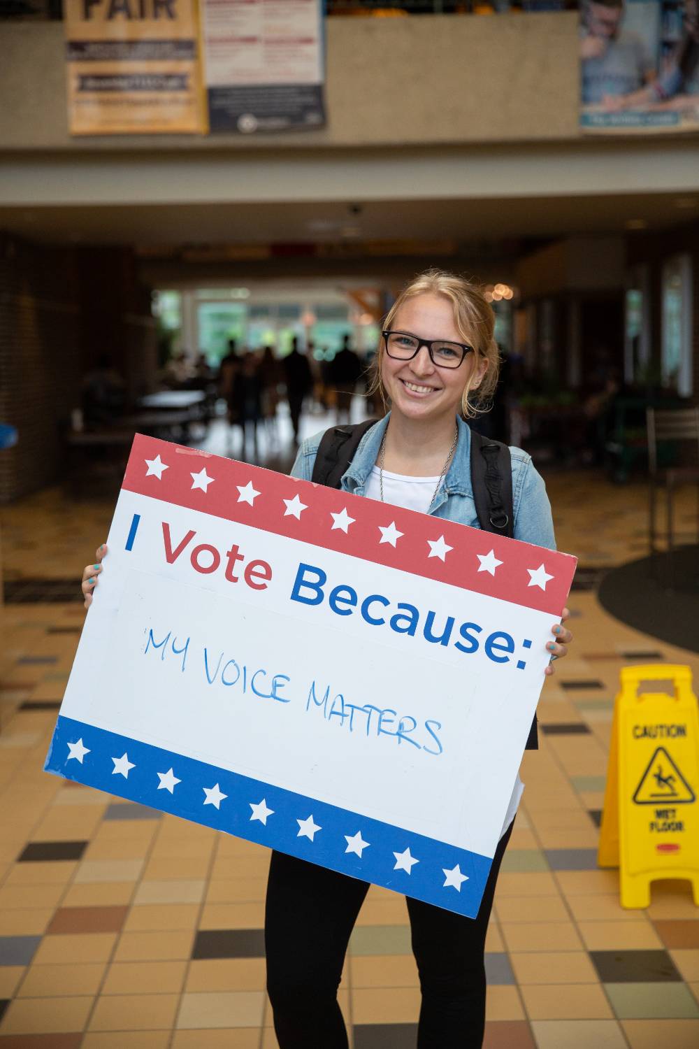 Student holding sign titled "I vote because: my voice matters"